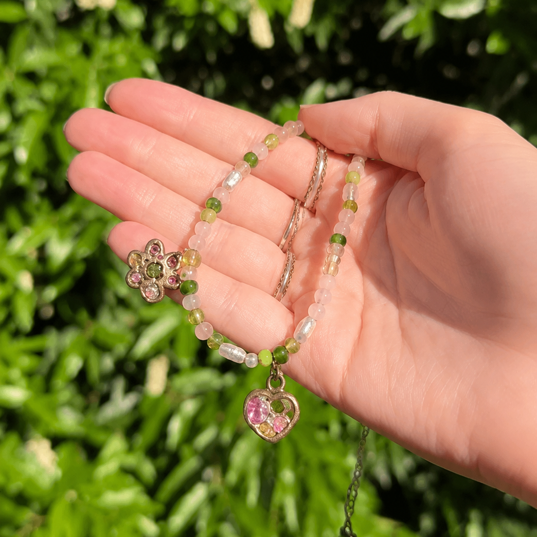 Hand holding a beaded bracelet with a heart charm against a green leafy background