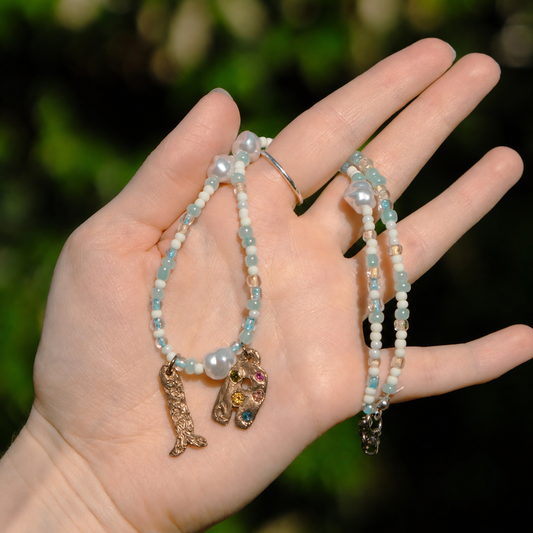 Hand holding two beaded bracelets with charms against a blurred natural background